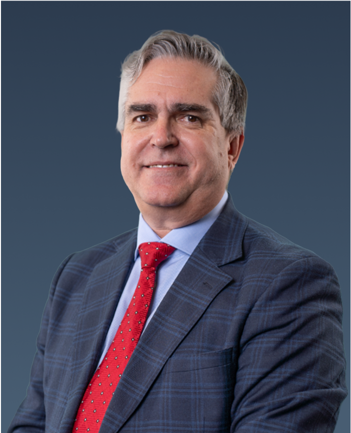 Professional portrait of a man with gray hair in a dark checkered suit and red tie, smiling.